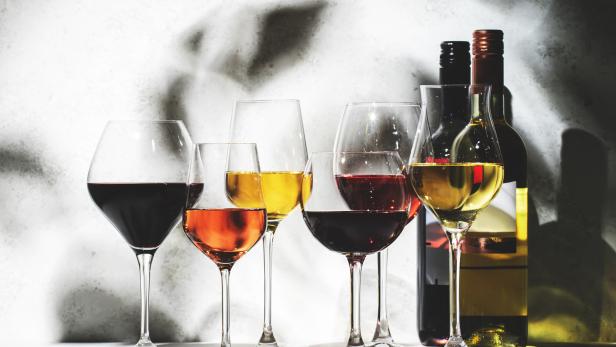 Mehrere Gläser mit Rotwein, Roséwein und Weißwein stehen vor Weinflaschen.