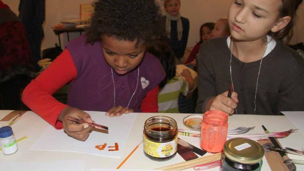 Zwei Mädchen bemalen mit Federn und Tinte Papierbögen.