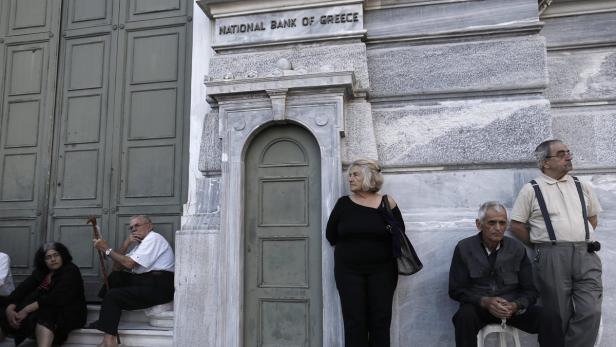 Eine Gruppe von Menschen sitzt und steht vor dem Gebäude der National Bank of Greece.