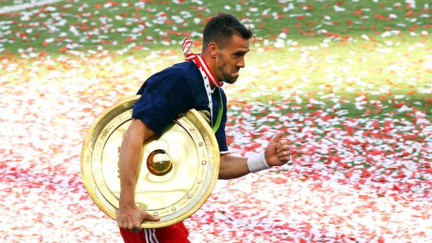 Ein Fußballspieler mit der Meisterschale inmitten von Konfetti.