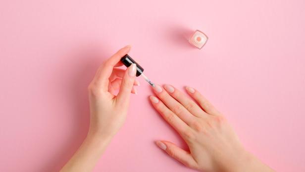 Eine Frau lackiert ihre Nägel auf einem rosa Untergrund.