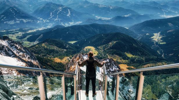 Ein Mann steht auf einer Aussichtsplattform und blickt auf die Berglandschaft.