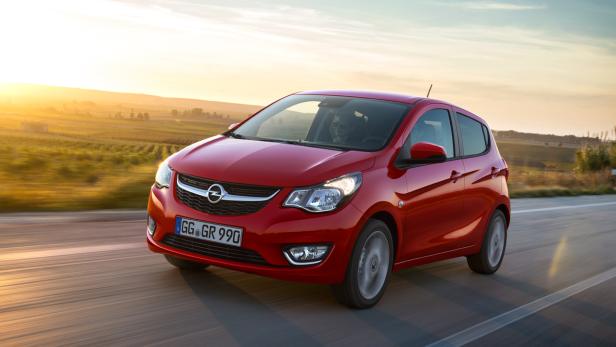Ein roter Opel Karl fährt auf einer Landstraße bei Sonnenuntergang.