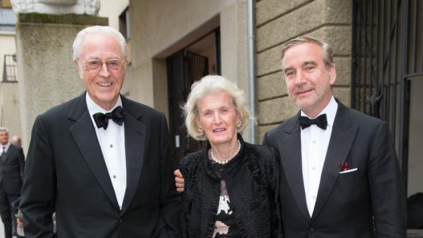 Drei Personen in formeller Kleidung posieren für ein Foto vor einem Gebäude.