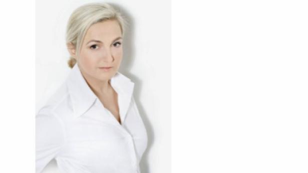 Eine Frau mit blonden Haaren und weißem Hemd vor einer weißen Wand.
