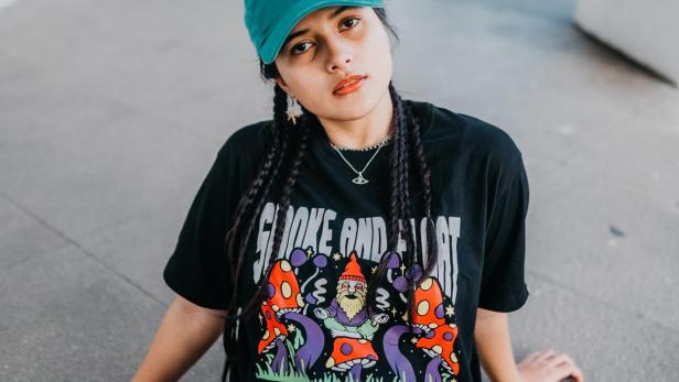 Eine junge Frau mit Zöpfen und einem T-Shirt mit Pilzmotiv sitzt auf dem Boden.