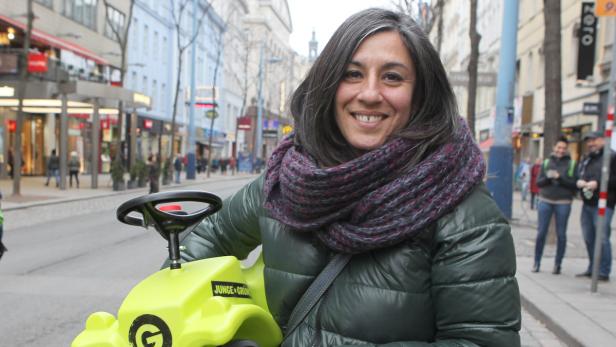 Eine Frau lächelt, während sie auf einem gelben Rutschauto auf einer belebten Straße sitzt.
