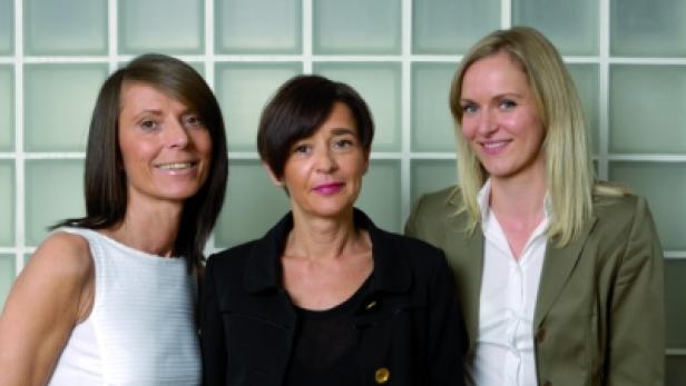Drei Frauen stehen vor einer Wand aus Glasbausteinen.