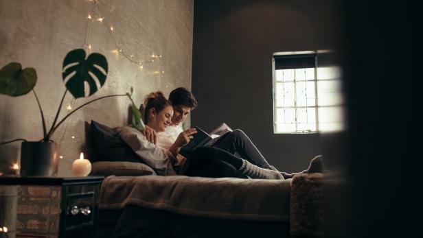 Ein Paar liest gemeinsam ein Buch im Bett, umgeben von warmem Licht.
