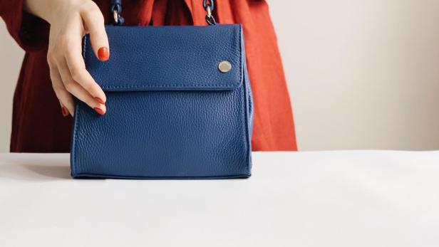 Eine Frau im roten Kleid hält eine blaue Ledertasche.