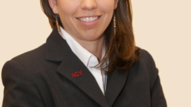 Eine Frau mit braunen Haaren trägt einen schwarzen Blazer mit dem ACV-Logo.