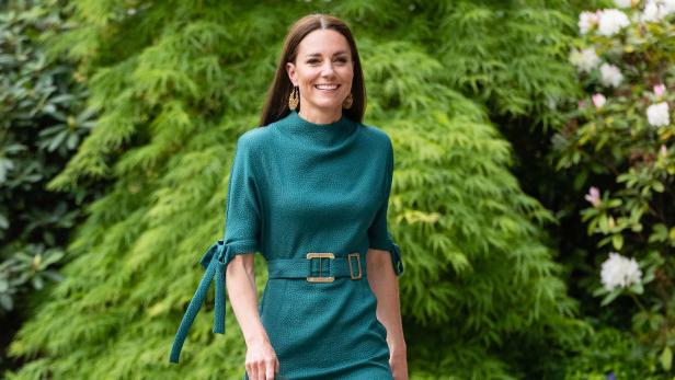 Catherine, Prinzessin von Wales, in einem grünen Kleid mit goldenen Ohrringen vor einem grünen Hintergrund.