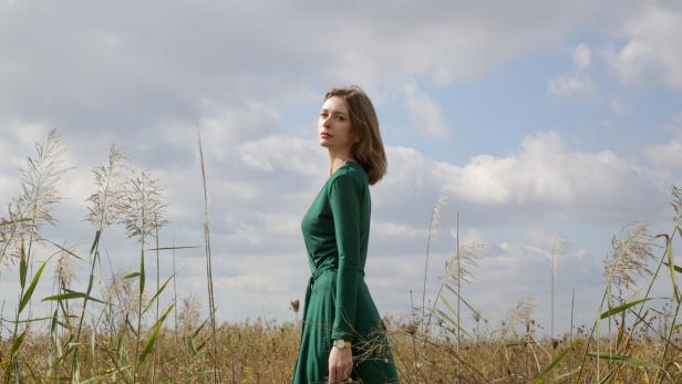 Eine Frau in einem grünen Kleid steht in einem Feld mit hohem Gras.
