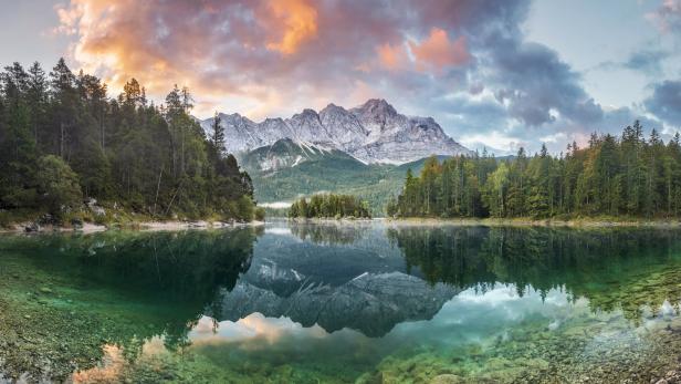 Der Eibsee spiegelt die Zugspitze und den bewaldeten Uferbereich wider.