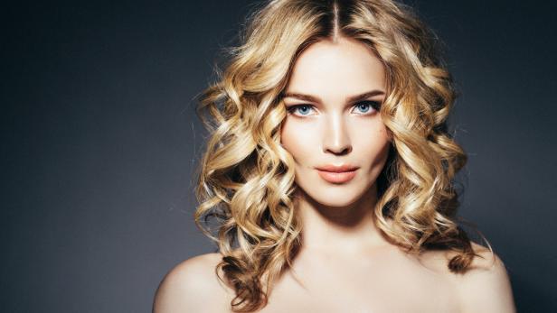 Porträt einer Frau mit blonden Locken und einem grünen, paillettenbesetzten Kleid.