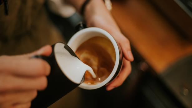 Jemand gießt Milch in eine Tasse Kaffee.