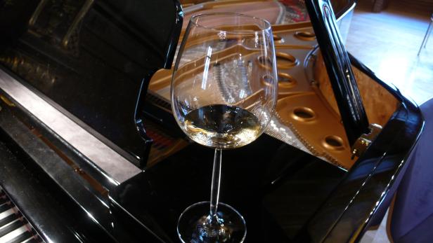 Ein Glas Weißwein steht auf einem schwarzen Klavier.