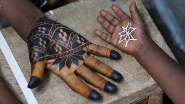 Eine Hand ist mit traditioneller schwarzer Henna-Kunst verziert, eine andere mit einem weißen Muster bemalt.