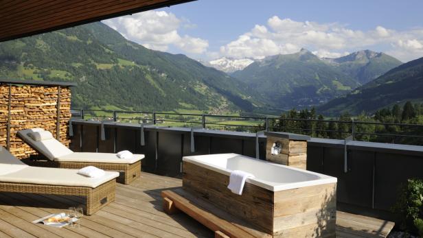 Auf einer Terrasse stehen zwei Liegen und eine Badewanne mit Blick auf die Berge.