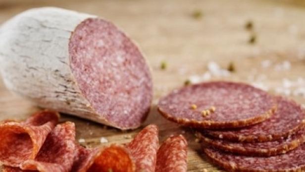 Eine Salami liegt zusammen mit einigen Salamischeiben auf einem Holzbrett.