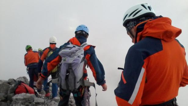 Eine Gruppe Bergsteiger mit Helmen und Rucksäcken wandert durch nebliges Gelände.