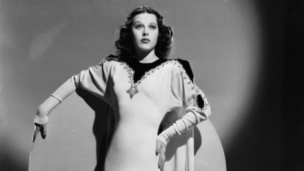 Hedy Lamarr posiert in einem langen, hellen Kleid vor einem runden Hintergrund.