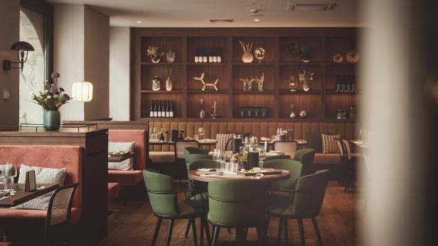 Ein elegantes Restaurant mit Tischen, grünen Stühlen und einer Wand mit dekorativen Objekten.