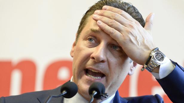 Ein Mann in einem Anzug gestikuliert mit der Hand an der Stirn vor Mikrofonen.