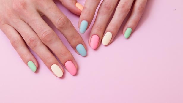 Hände mit pastellfarben lackierten Fingernägeln auf rosa Hintergrund.