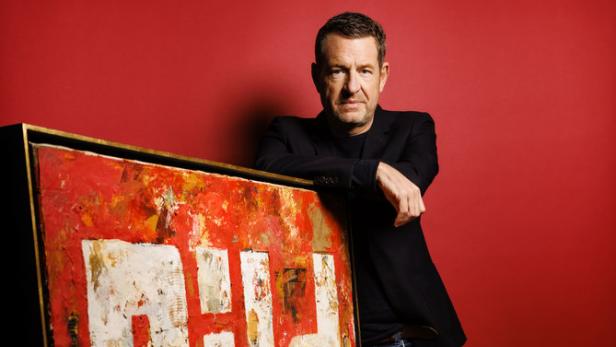 Ein Mann lehnt an einem großen, abstrakten Gemälde mit roten und weißen Elementen.