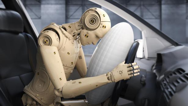 Ein Crash-Test-Dummy sitzt in einem Auto, der Airbag hat sich geöffnet.