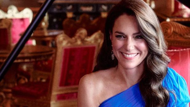 Kate Middleton lächelt in einem blauen Kleid an einem Klavier sitzend.