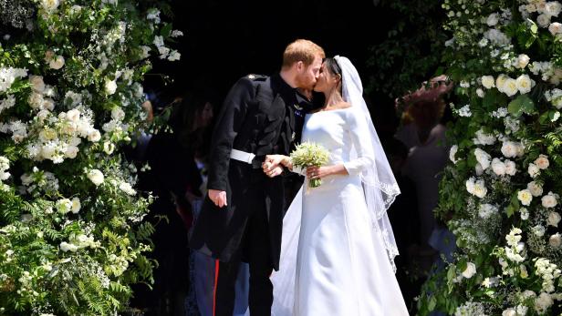 Prinz Harry und Meghan Markle küssen sich nach ihrer Hochzeit vor einem mit Blumen geschmückten Eingang.