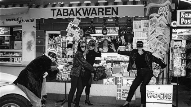 Vier Frauen mit Masken posieren vor einem Tabakwarenladen in Schwarzweiß.