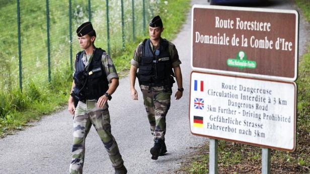 Zwei französische Gendarmen patrouillieren auf einer Straße in der Nähe eines Schildes, das auf eine gefährliche Straße hinweist.
