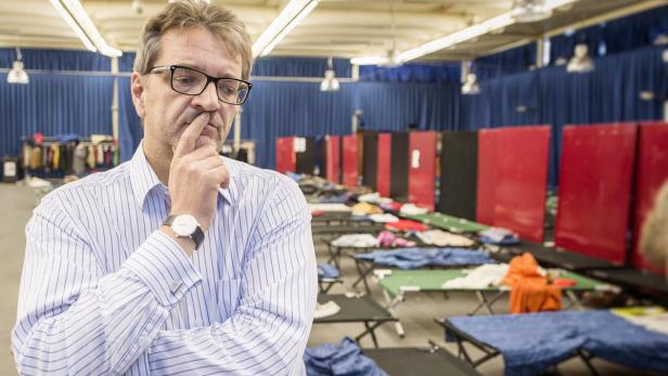 Ein nachdenklicher Mann steht vor Feldbetten in einer Notunterkunft.