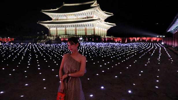 Eine Frau posiert vor dem Gyeongbokgung-Palast, der nachts beleuchtet ist.