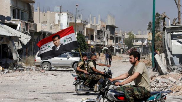 FILE PHOTO: Forces loyal to Syria's President Assad carry the national flag as they ride on motorcycles in Qusair