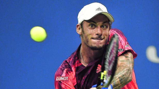 Ein Tennisspieler schlägt einen Ball vor einem blauen Hintergrund.