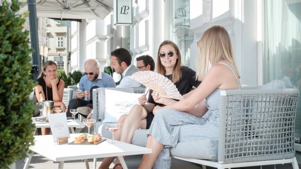 Eine Gruppe von Menschen sitzt in einem Straßencafé und genießt Getränke und Snacks.