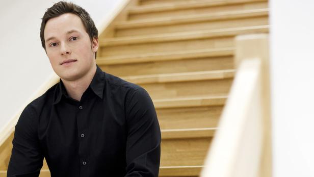 Ein Mann mit schwarzem Hemd sitzt auf einer hellen Holztreppe.