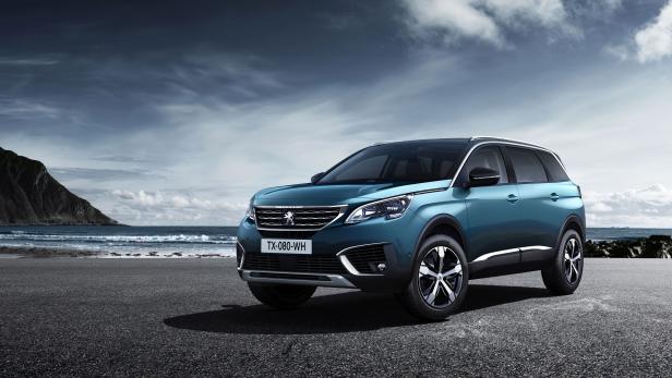 Ein türkisfarbener Peugeot SUV steht vor einer Küstenlandschaft.
