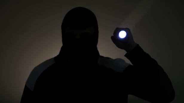 Blurred photo. Burglar in dark clothes holding the flashlight. Dangerous robber in mask with a torch. Criminal man.