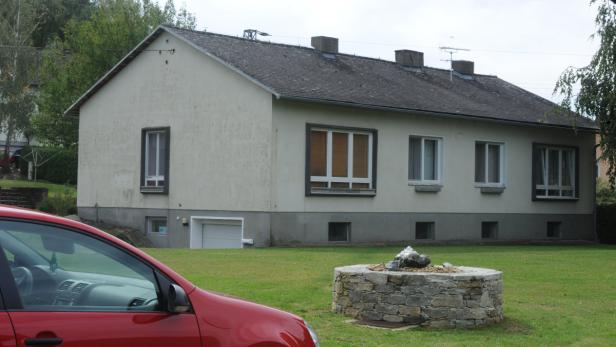 Ein zweistöckiges Haus mit einem Steingarten und einem roten Auto im Vordergrund.