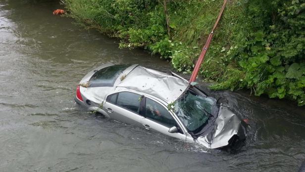 Ein silbernes Auto liegt nach einem Unfall beschädigt in einem Fluss.