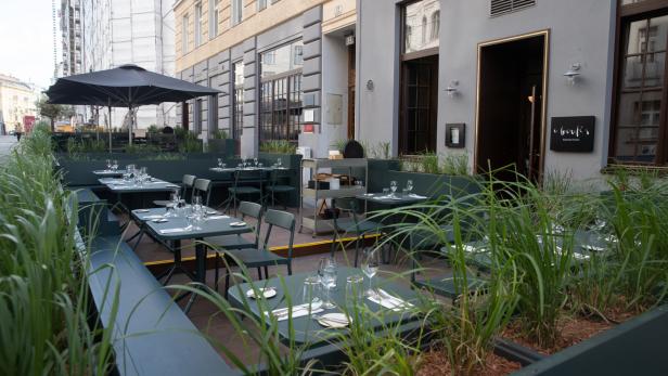 Das Restaurant „O boufés“ mit Tischen im Freien und viel Grün im Außenbereich.