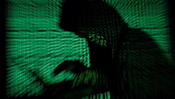 Person mit Kapuze vor Computer, grüner Hintergrund mit Codes.