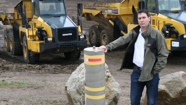 Ein Mann posiert vor zwei gelben Muldenkippern der Marke Komatsu.