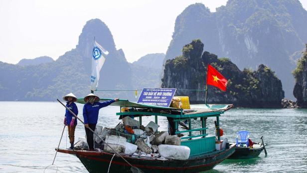 Zwei Frauen in traditionellen Hüten sammeln Müll mit einem Boot in Vietnam.
