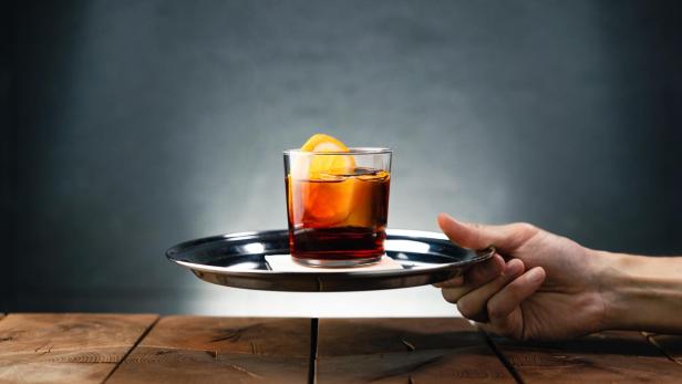 Ein Negroni Sbagliato mit einer Orangenscheibe wird auf einem Tablett serviert.